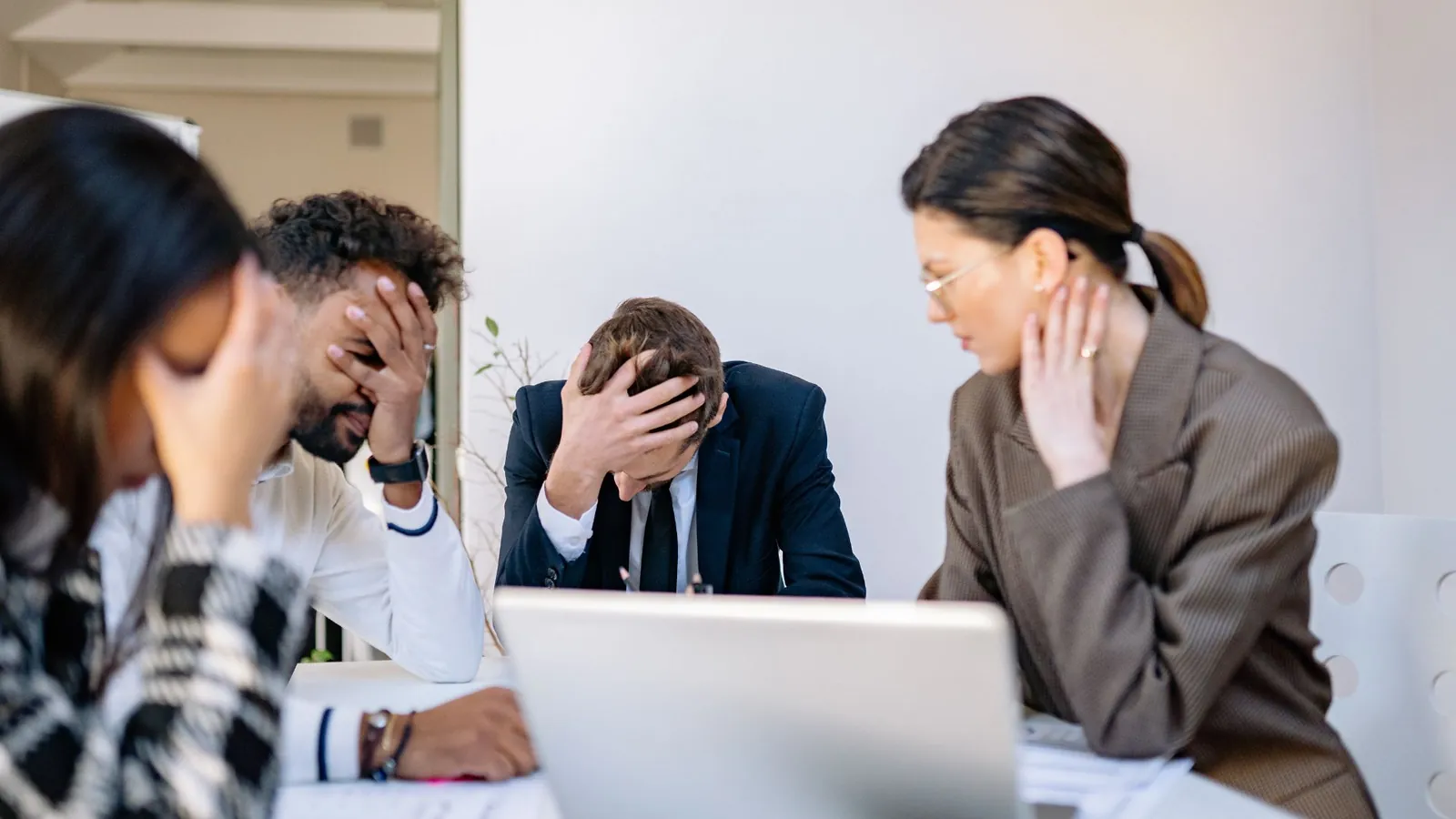 A team holding their heads in frustration around a meeting table